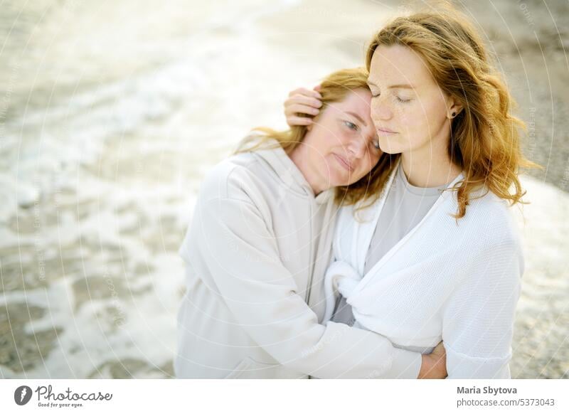 Redhead senior mother and her beautiful adult daughter are walking together and embracing. Family relationships between adult children and older parents similar