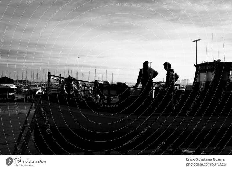 Two men on a wooden boat out of the water in the port of Punta del Este, Uruguay. human black and white ship high contrast street photography fishermen Port