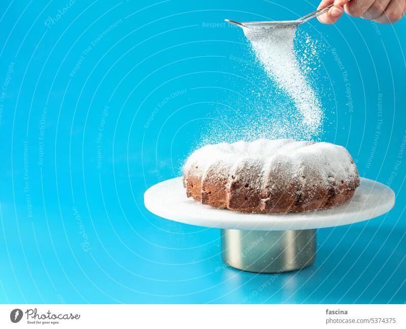 Female hand sprinkling icing sugar on bundt cake bunt cake falling home made blue homemade copy space sugar falling cake snow fresh gourmet sweet dessert food