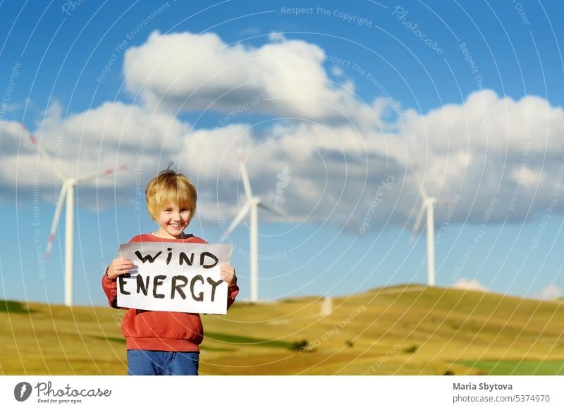 Eco activist boy with banner "Wind Energy" on background of power stations for renewable electric energy production. Child and windmills. Wind turbines for generation electricity. Green energy