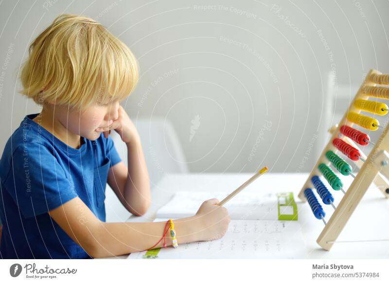 Elementary student boy doing homework at home. Child learning to count, solves arithmetic examples, doing exercises in workbook. Math tutorial. Preparing preschooler baby for school. Education