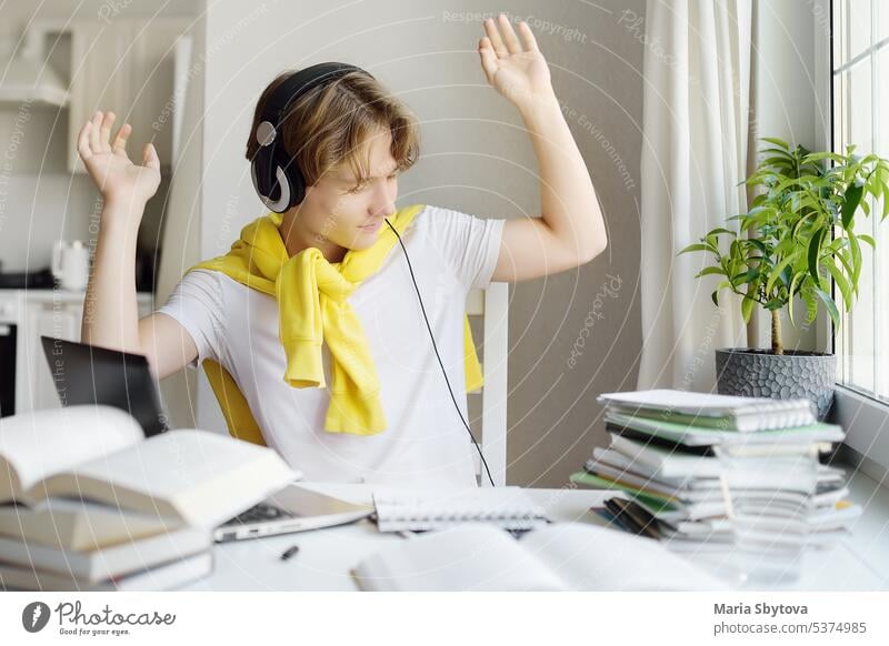 Teenager boy study at home using gadgets. Online education and distance learning for children. High school student wearing headphone listening music, dancing and joy because homework test done.