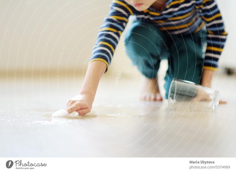 Little boy wipes water spilled from a glass on the floor. Teaching a child to clean up after himself. Responsibility, accuracy. Help around the house. Household duties.