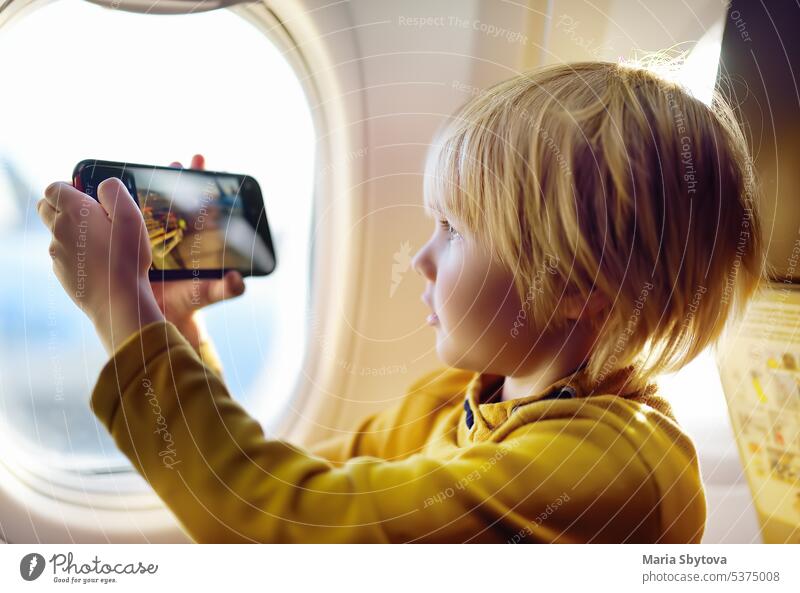 Little boy is taking a shot view of airfield from illuminator plane by smartphone. take aircraft blogger photographer videographer airplane travel little window