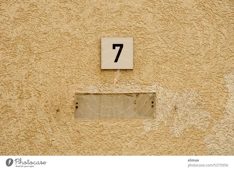 small sign with a 7 under which another sign was visually removed on a plastered beige house wall for hire Number 7 Name plate Blog Plaster digit