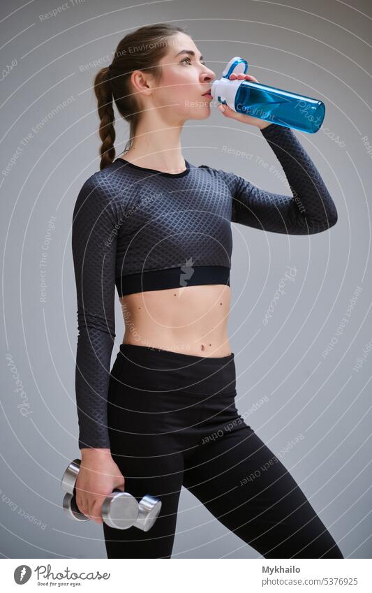 Beautiful young girl in sportswear with dumbbells drinks water in the gym. The girl does sports training, sports. Fitness woman work slim mat aerobics bottle