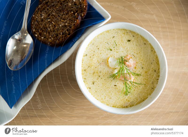 A bowl of Finnish Lohikeitto soup served on wooden table with a piece of Swedish rye bread. Creamy broth, tender potatoes, and flaky pink salmon create a delicious dish.