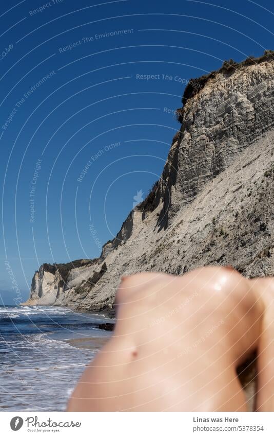 It’s a wonderful beach in Corfu, Greece. A wild coastline and calm sea. A blue sky. And a gorgeous nude girl who is out of focus. Her sexy blurred lines are undeniable though. A young and naked woman is enjoying the hot summer obviously.