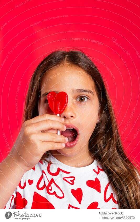 Surprised girl with open mouth licking lollipop with red heart surprise amazed confuse sweet candy portrait mouth opened puzzle kid bewilder wonder dessert