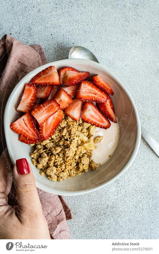 Cropped hand holding bowl with healthy breakfast with strawberries, yogurt and granola woman background berry cereal concept concrete diet eat eating food fruit