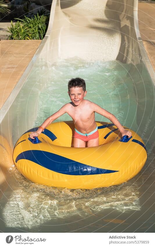Happy child standing on a ring on the water slide having fun enjoy park wet hair inflatable smile kid boy summer weekend childhood carefree happy playful