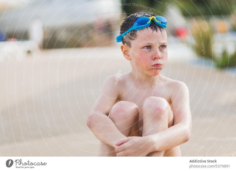 Child sitting on the blurred ground of the park kid focus shirtless calm goggles cute wet bare shoulders summer child boy recreation weekend daytime childhood