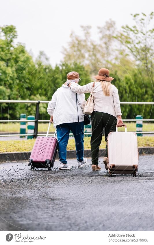 Anonymous senior women with suitcases walking hugging along road traveler embrace trip luggage vacation together journey elderly summer friend holiday move calm