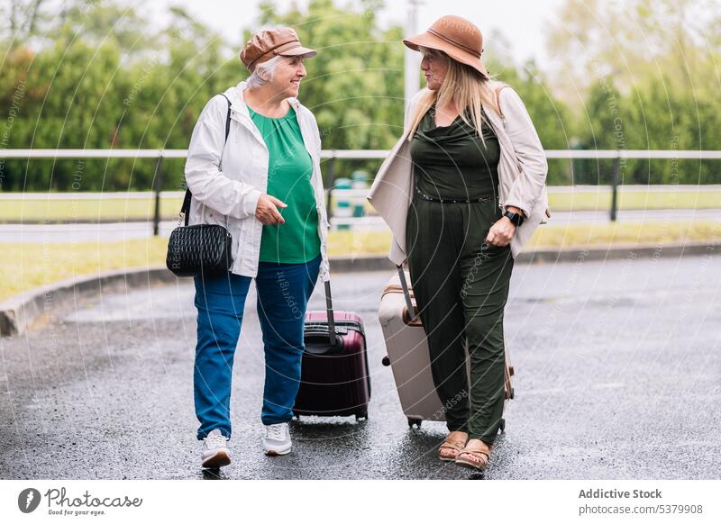 Happy senior women with suitcases walking along road traveler trip luggage vacation together talk smile journey elderly summer friend holiday cheerful road trip