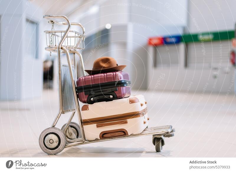 Trolley with suitcases and hat in airport terminal luggage trip travel modern cart departure vacation colorful baggage journey flight contemporary trolley