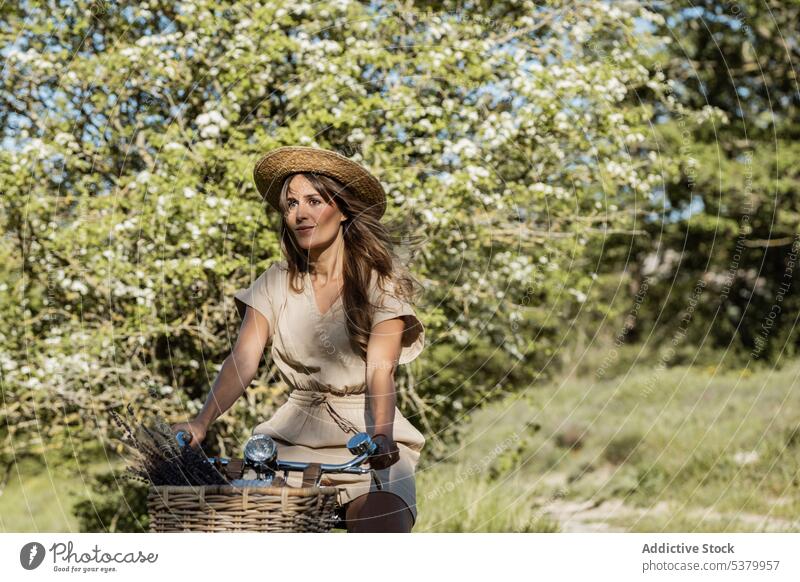 Woman riding bicycle in countryside woman ride nature summertime carefree fun happy female straw hat overall style rural long hair natural grassy fresh flower