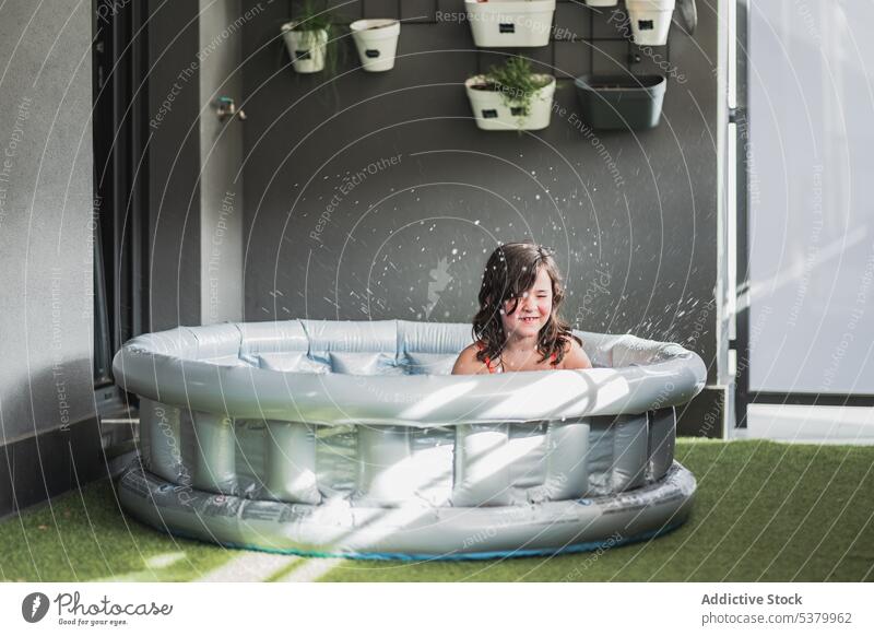 Smiling child sitting in pool in room kid inflatable water grass having fun happy wall mat smile preteen enjoy childhood hang girl eyes closed plant bath