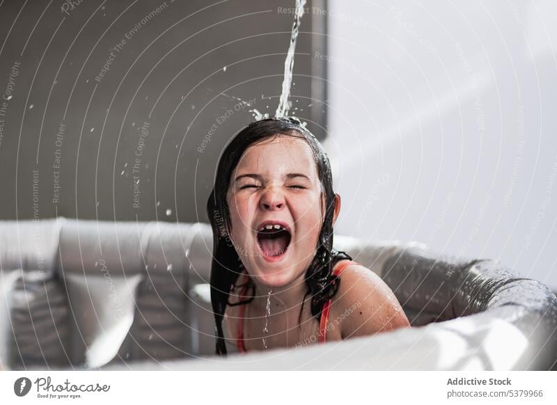 Excited kid screaming in children pool with eyes closed girl water mouth opened having fun happy play wet hair shout yell bathtub excited playful enjoy cheerful