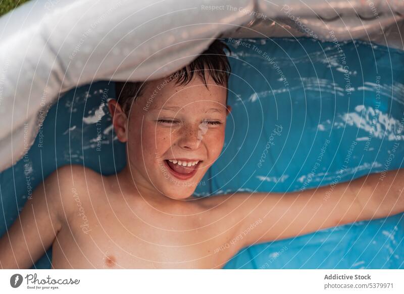 Happy shirtless kid lying in pool with blue water child relax smile bathtub cheerful positive enjoy hygiene boy weekend toothy smile happy chill childhood