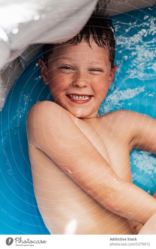 Cheerful shirtless kid lying in pool with blue water child relax smile bathtub cheerful positive enjoy hygiene boy weekend toothy smile happy chill childhood