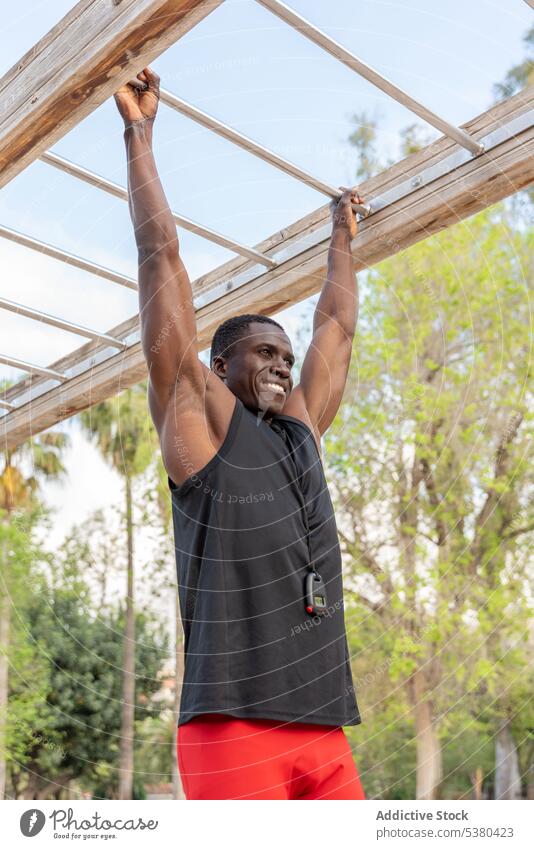 Happy black man hanging on bar in sports ground workout training pull exercise athlete strong african american ethnic street fitness happy male young power