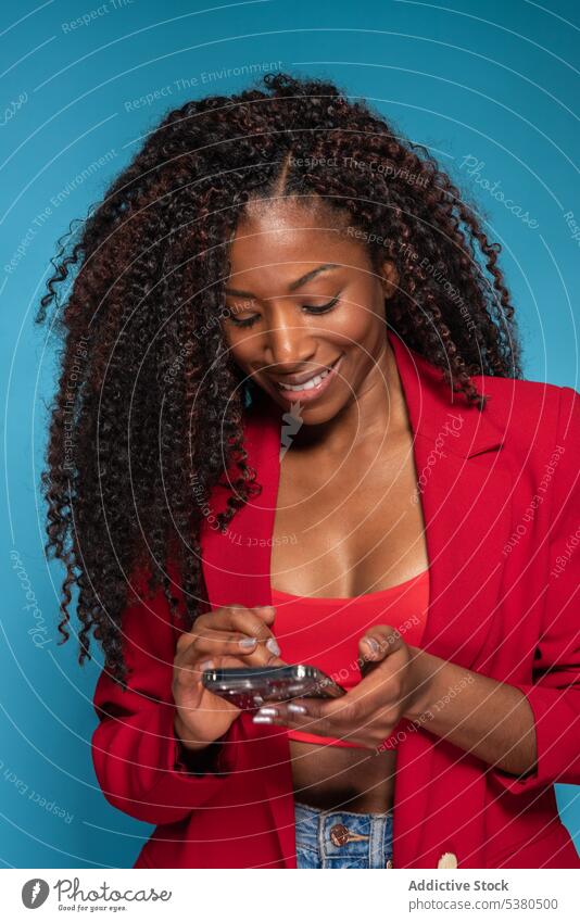 Smiling woman in red outfit sending message talk smartphone smile fashion style black female texting young conversation happy afro using device mobile gadget