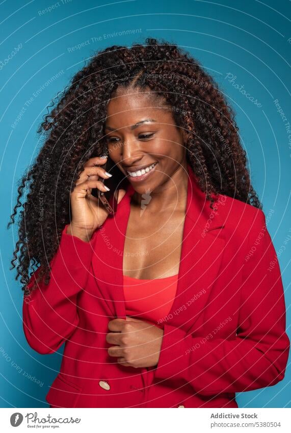 Smiling woman in red stylish clothes talking on smartphone phone call smile speak fashion style black female young outfit cheerful conversation happy afro using