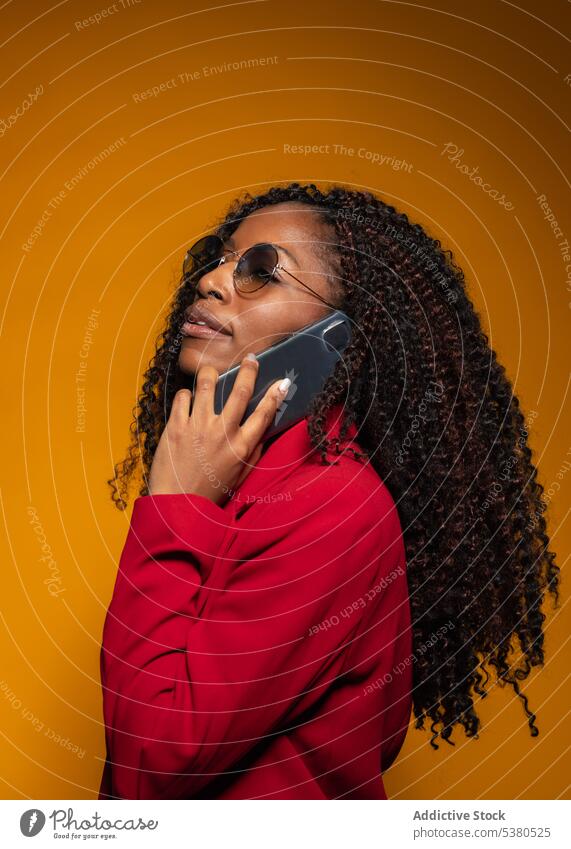 Thoughtful lady speaking on smartphone in studio woman conversation phone call style trendy outfit positive talk female african american black young eyeglasses