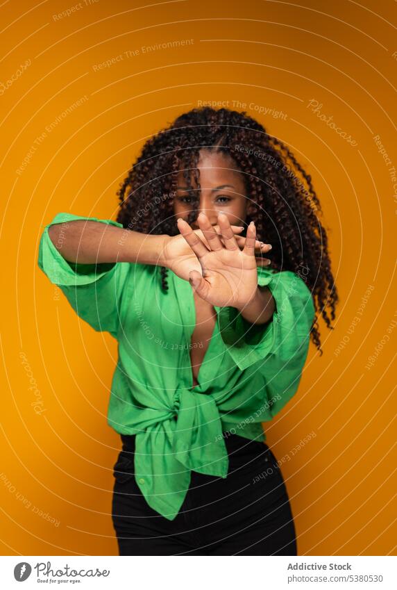 Trendy black woman with raising arms in studio gesture sign curly hair trendy modern style symbol casual mouth cover female young african american lady model