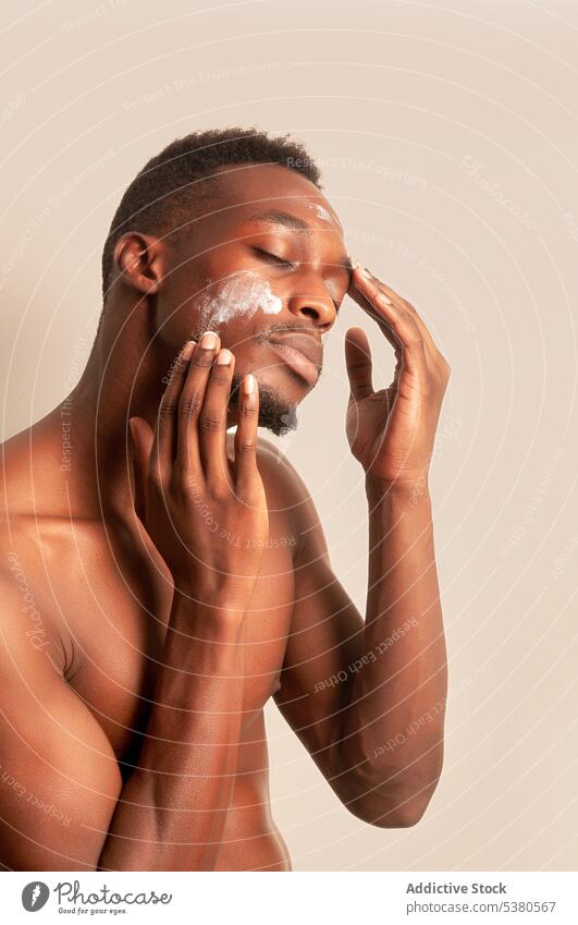 Shirtless black man applying cream on face skin care daily moisture cosmetology procedure facial routine treat male beauty calm wellness cosmetic pamper