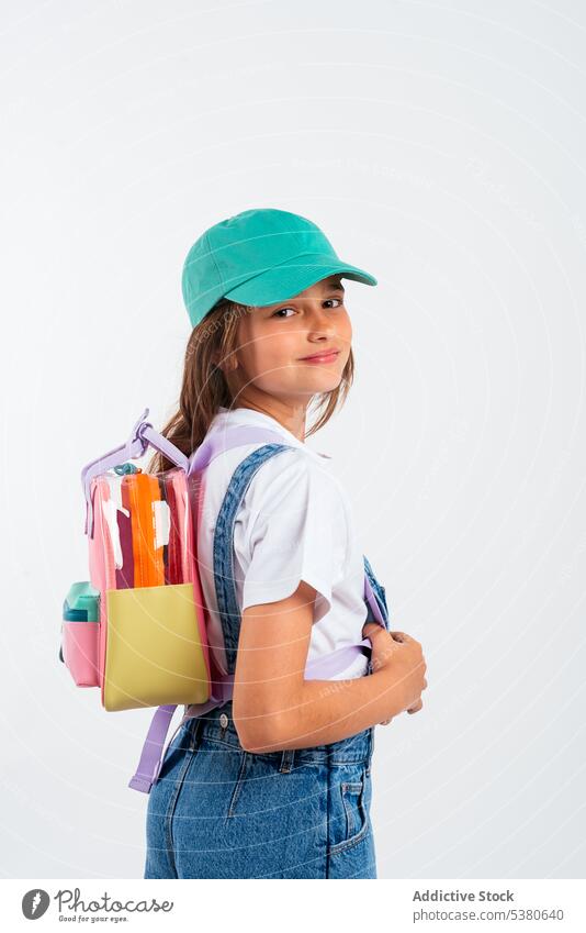Smiling schoolgirl with backpack and cap calm kid child little smile style hat childhood happy positive education studio shot preschool elementary glad primary