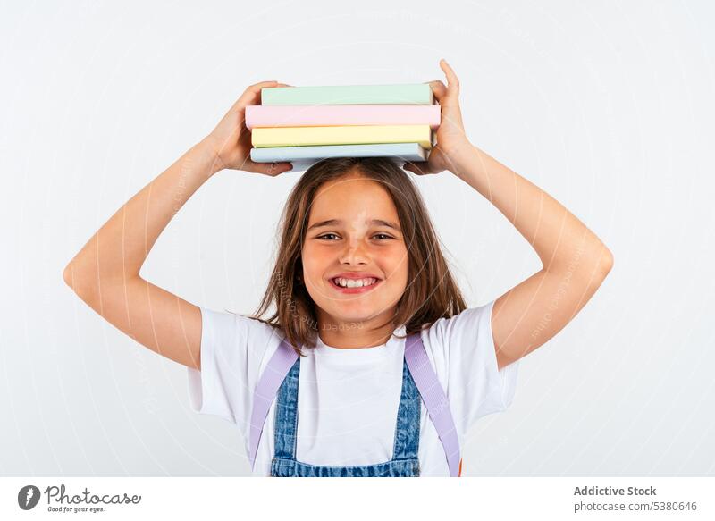 Cheerful schoolgirl with books on head kid colorful stack balance smile pile uniform child positive education pupil happy little apron knowledge literature glad