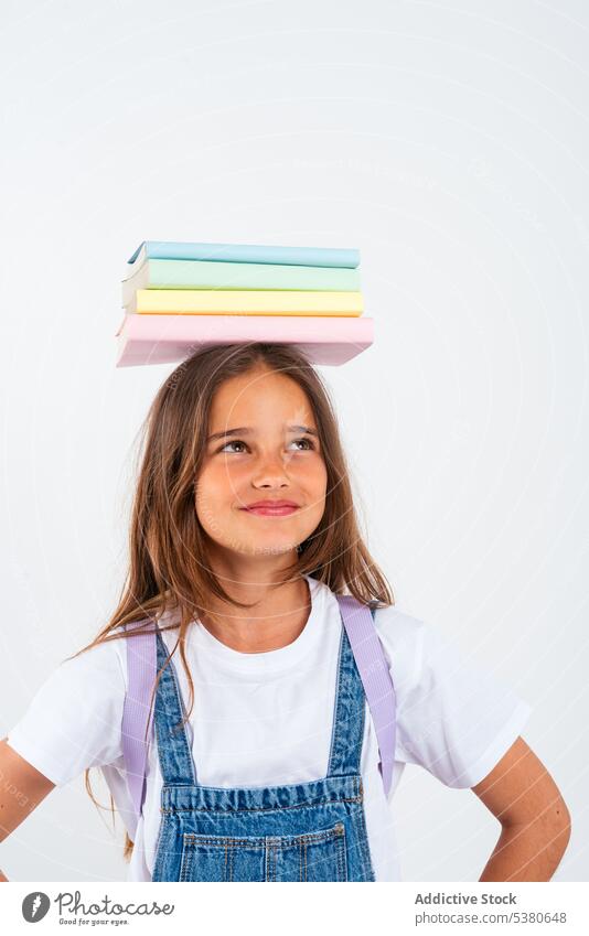 Smiling schoolgirl with books on head kid colorful stack balance smile pile uniform child positive education pupil happy little apron knowledge literature glad