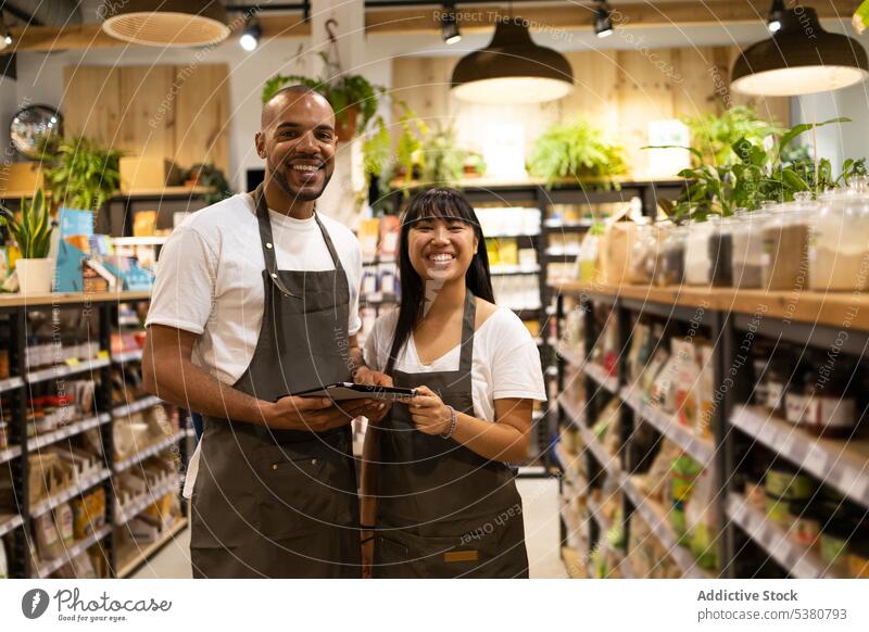 Ethnic sales staff checking information on tab in grocery shop woman tablet using shelf supermarket young team couple teamwork together ethnic gadget device