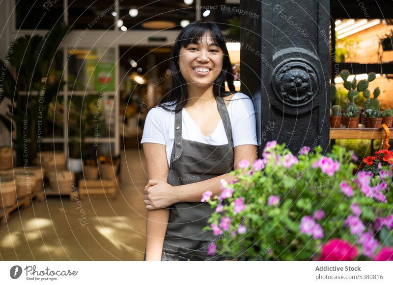 Cheerful Asian woman standing near blooming flowers florist smile floristry work shop owner counter bouquet female apron asian happy store job young