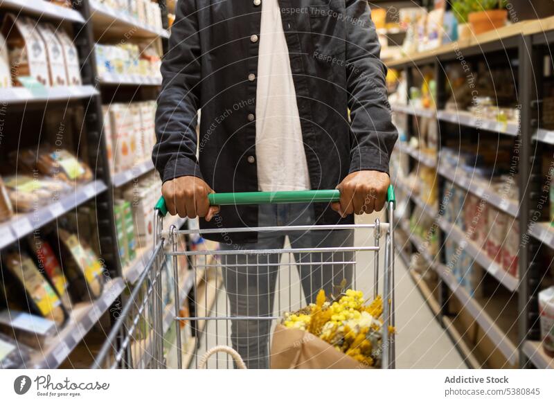 Unrecognizable black man with shopping trolley choosing products anonymous supermarket customer buy choose grocery purchase cart hypermarket food client store