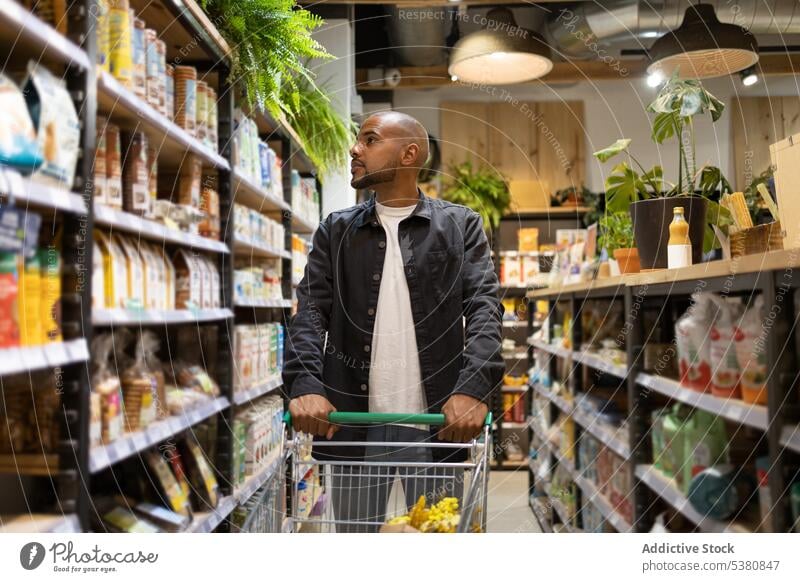 Black man with shopping trolley choosing products supermarket customer buy choose grocery purchase cart hypermarket food client store buyer male shelf