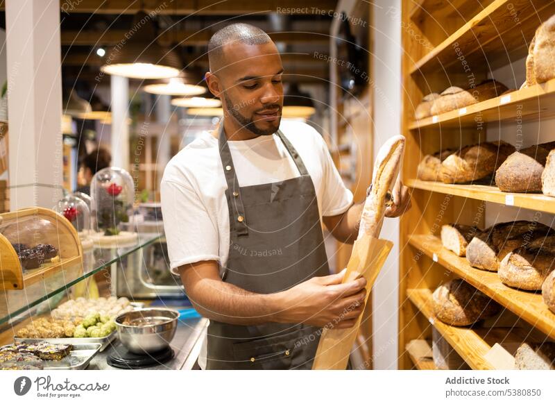 Serious black man putting bread in paper bag bakery seller grocery shop small business work baked owner food staff male ethnic pastry positive job serious store