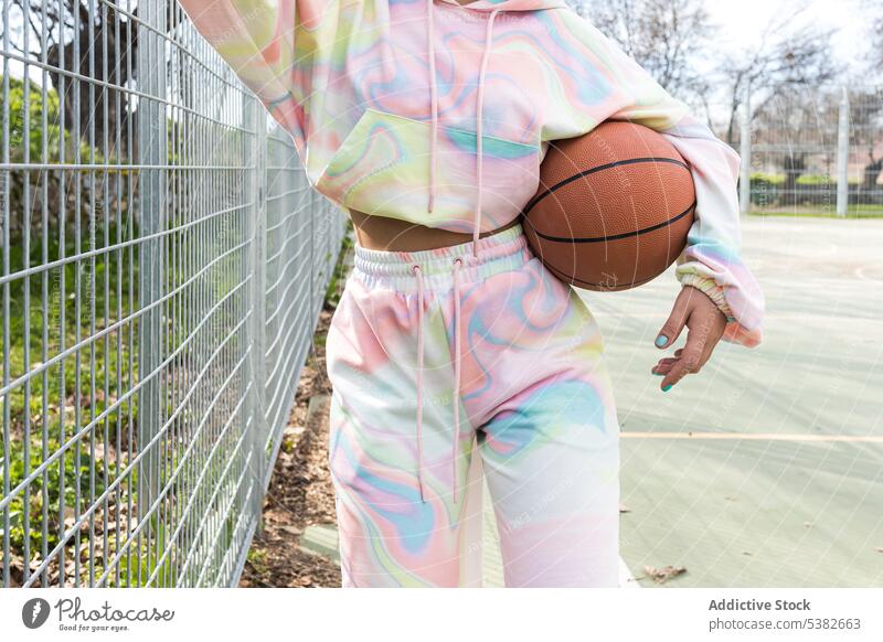 Anonymous woman with basketball standing near fence player sports ground hoodie practice athlete training daylight young female hobby activewear workout