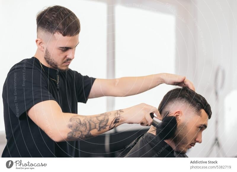 Young barber finishing haircut in hair salon barbershop beard bearded bearded man beauty care client clipping coiffure guy hairdresser hairstylist modern