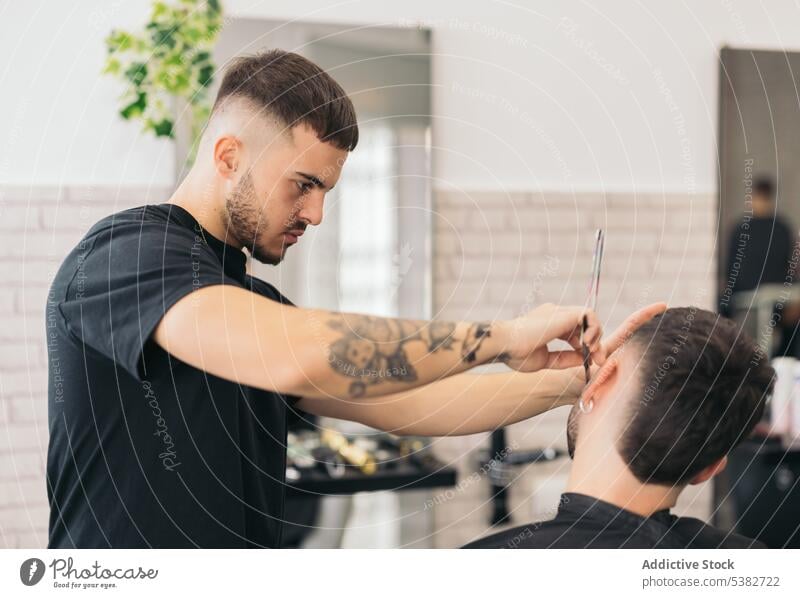 Young barber cutting beard with razor blade in hair salon barbershop bearded bearded man beauty care client clipping coiffure cutter guy haircut hairdresser