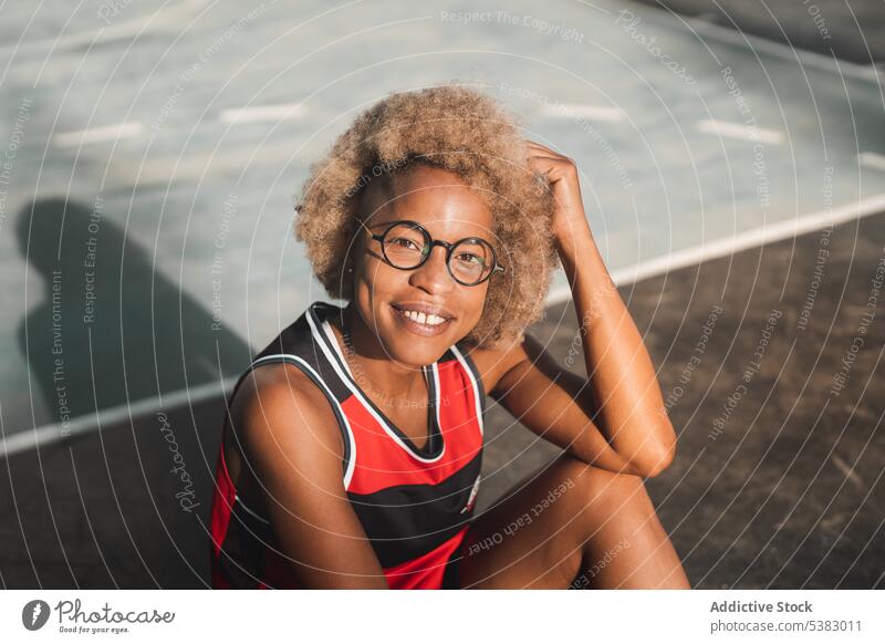 Cheerful black sportswoman resting on sports ground athlete basketball court sportswear cheerful happy sporty sneakers break african american sunset female