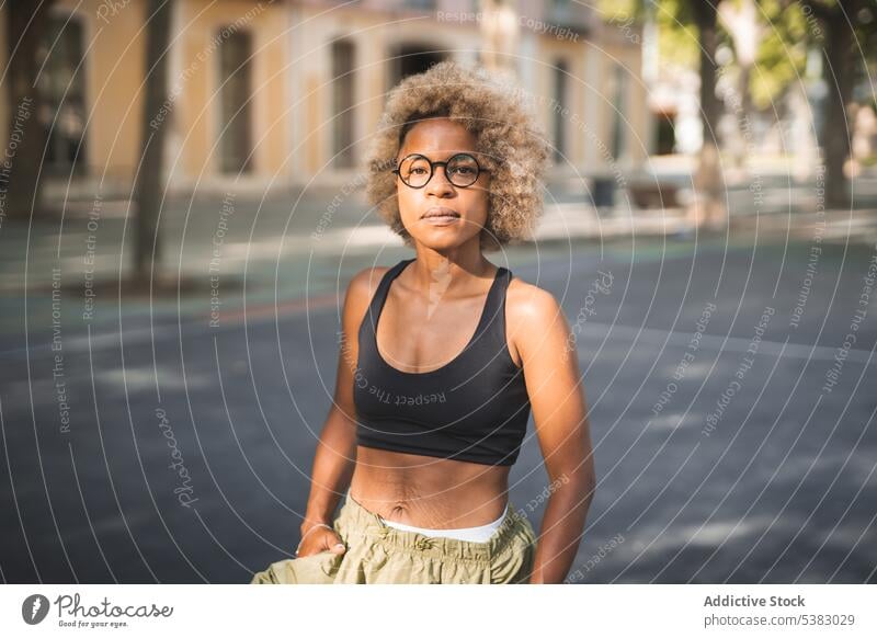 Serious black woman in sport bra and glasses standing on street cheerful curly hair sporty urban city african american young female ethnic daytime outside