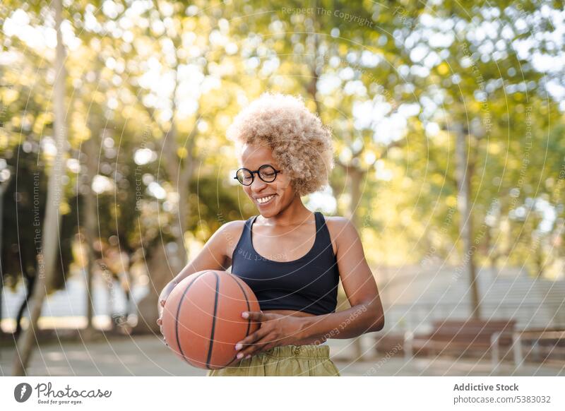 Cheerful young woman holding basketball while smiling in park player sport game sports ground athlete sportswoman african american black female court content