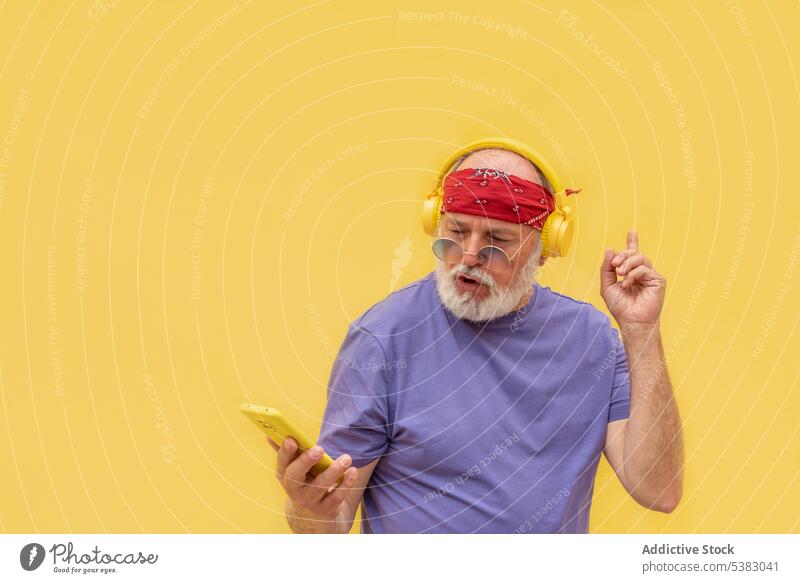 Senior man in headphones using smartphone music listen dance device gadget happy positive modern elderly male casual style sound song audio beard mobile melody