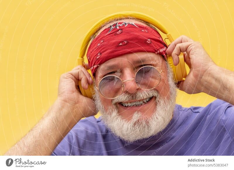 Happy man in headphones and eyeglasses listening to music cheerful hipster portrait happy gadget scarf positive tune senior beard male sound meloman elderly