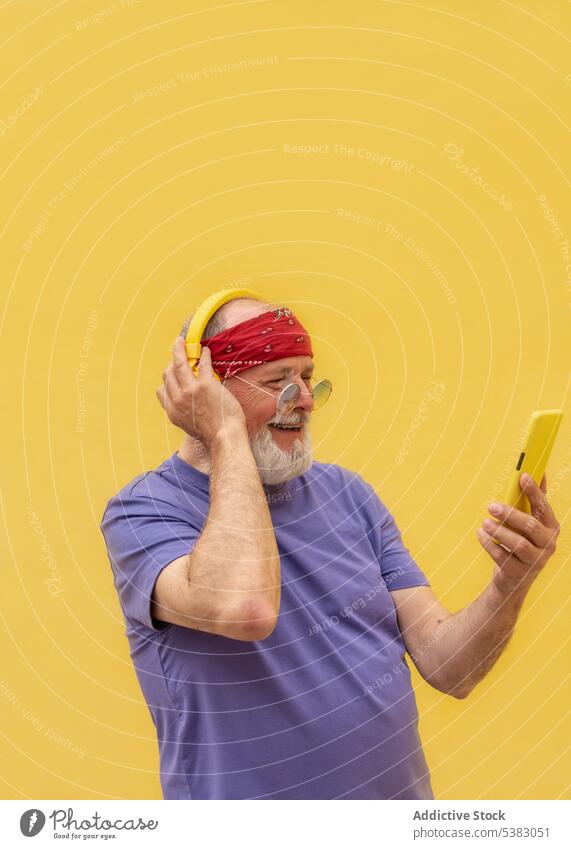 Side view senior man in headphones using smartphone music listen device gadget happy positive modern smile elderly male casual style sound song audio beard