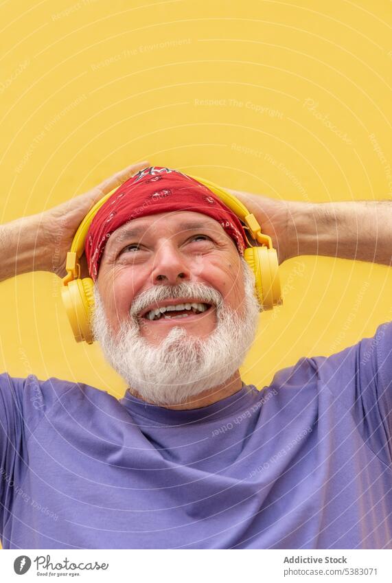Happy man in headphones listening to music cheerful hipster portrait happy gadget scarf positive tune senior old beard male sound meloman elderly device trendy