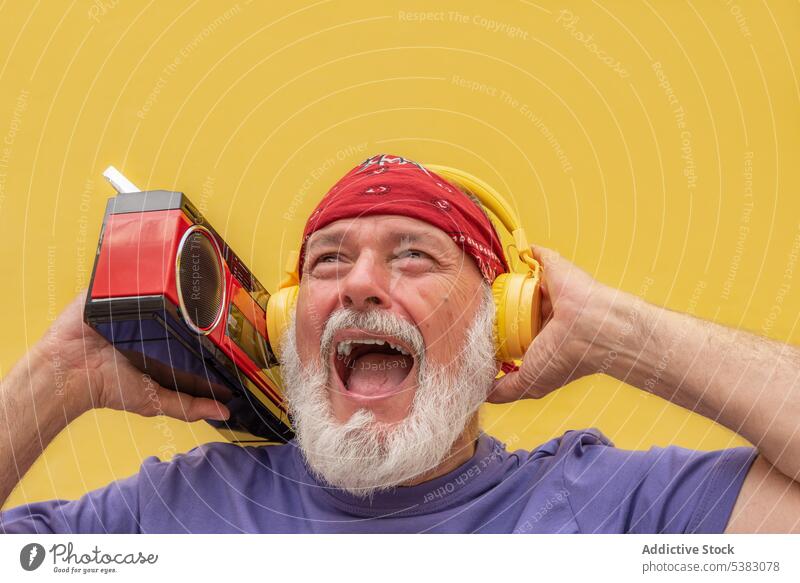 Excited senior man with headphones listening to music portrait cassette gesture device scream shout gadget sound aged voice beard song audio studio elderly male