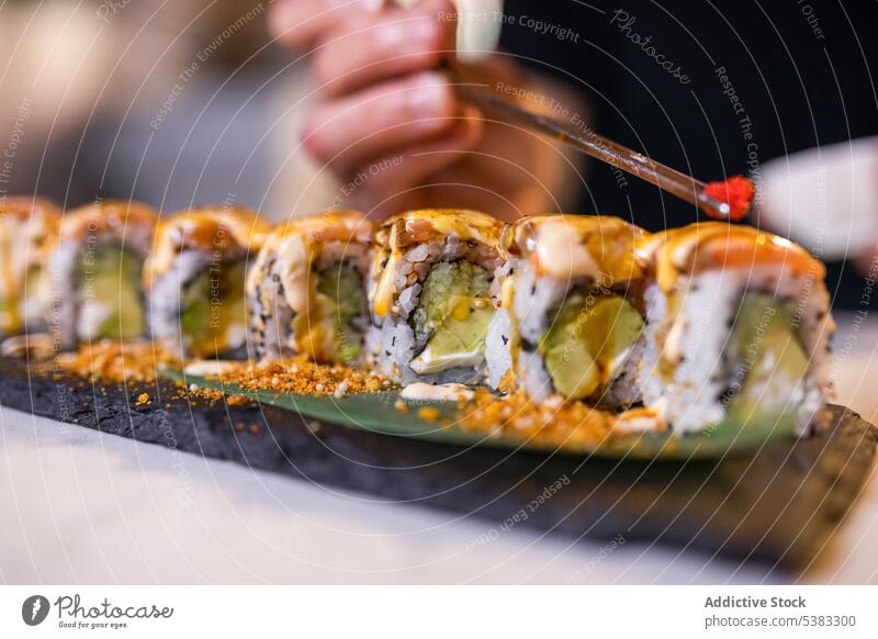 Unrecognizable person serving tobiko on uramaki sushi rolls with chopsticks rice serve seafood tray delicious avocado asian food meal tasty cuisine wooden
